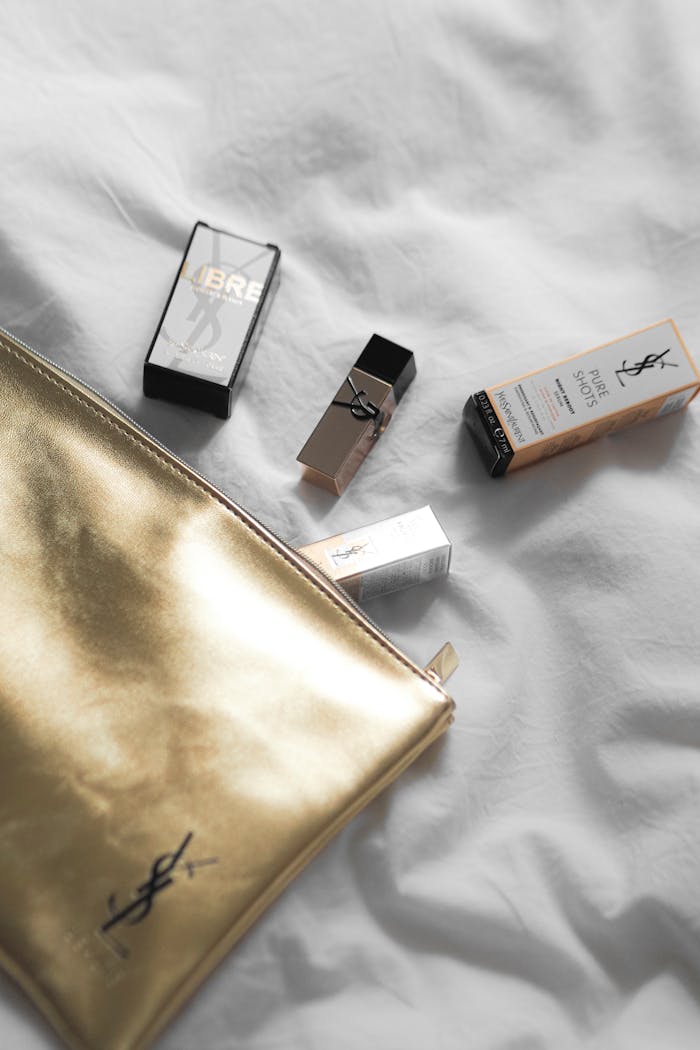 Elegant flat lay of Yves Saint Laurent beauty products with a golden pouch on soft white fabric.